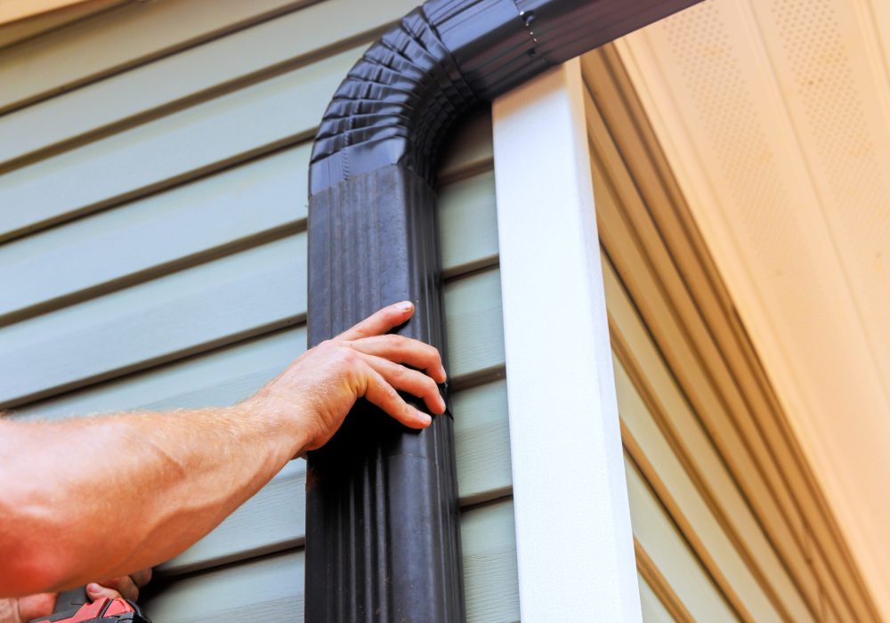 On roof, worker is installing rain gutter fitting downpipe downspout bend